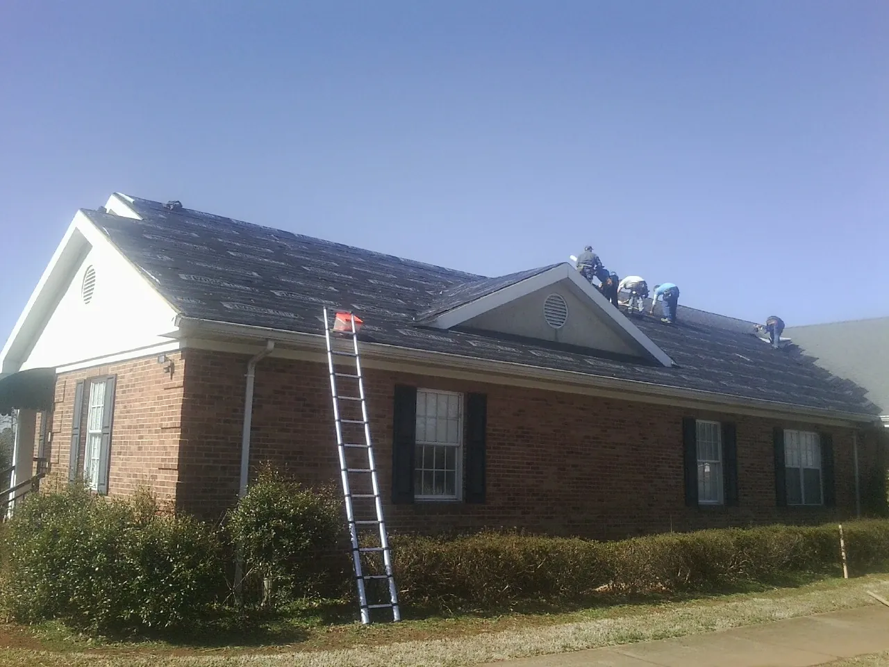 Crew tearing shingles off a brick ranch roof with a ladder set — Metal Roof Repair work by our crew in Indian Orchard