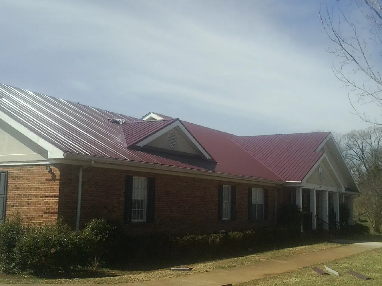 Red metal roof with gabled entries on a long brick building, from a Hail Damage Roof Repair job in Indian Orchard