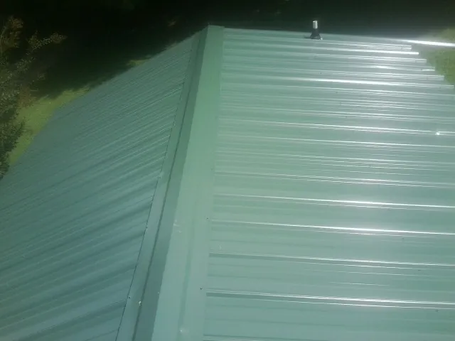 New green metal panels meeting at the ridge of a roof — Flat Roof Repair work by our crew in Indian Orchard