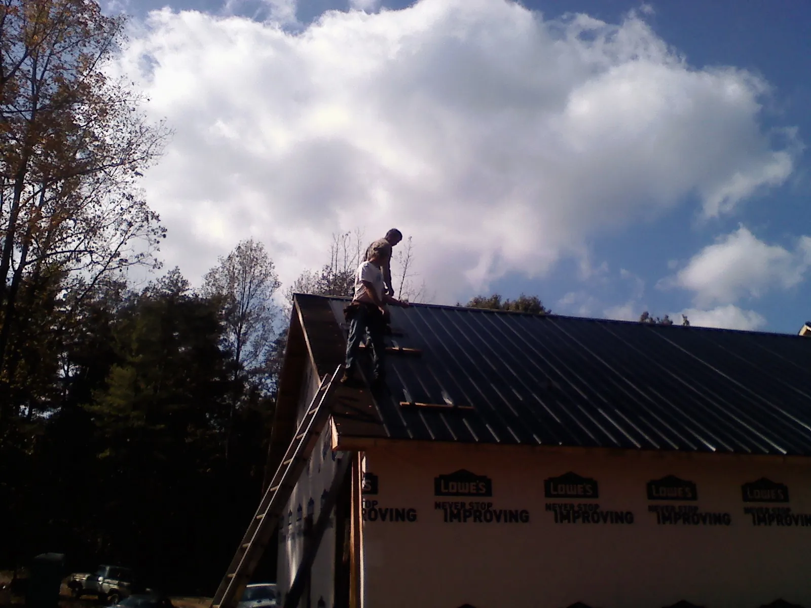 Roofer fastening dark metal panels high against a cloudy sky, from a Roof Inspection job in Indian Orchard