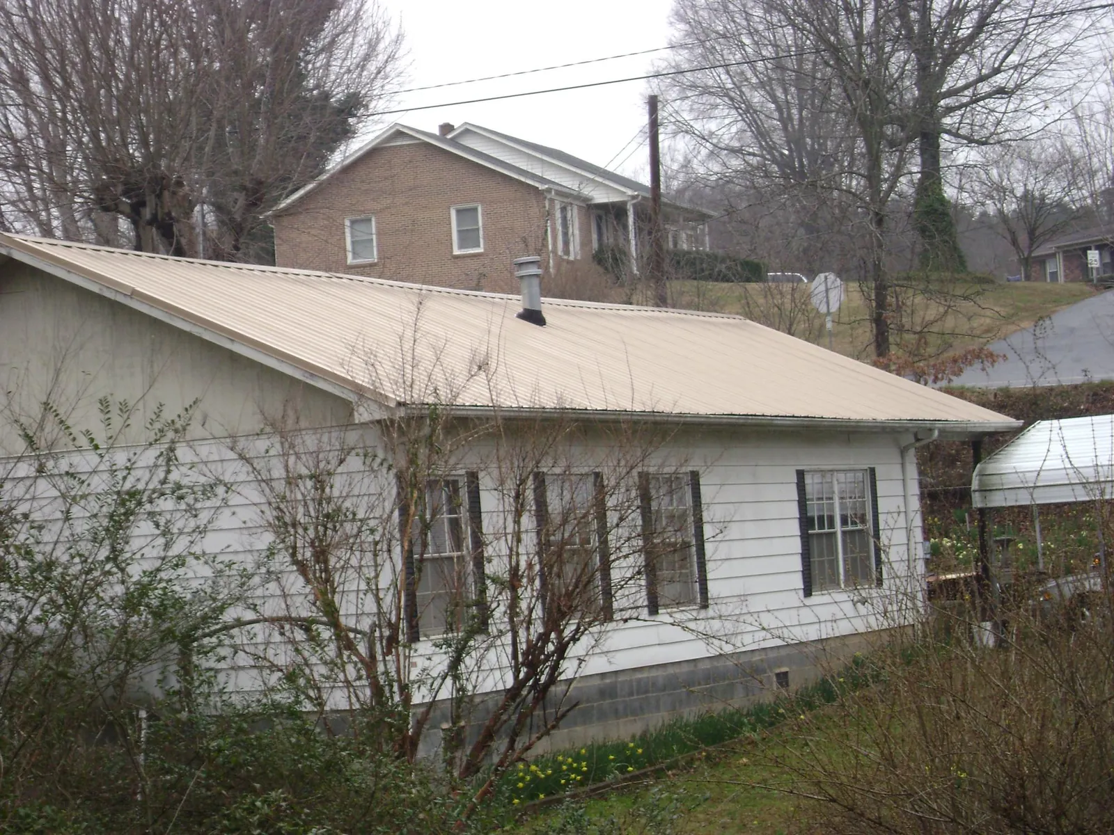 Tan metal roof on a white sided house set into a hillside — Commercial Roofing by Roofing Brothers in Indian Orchard